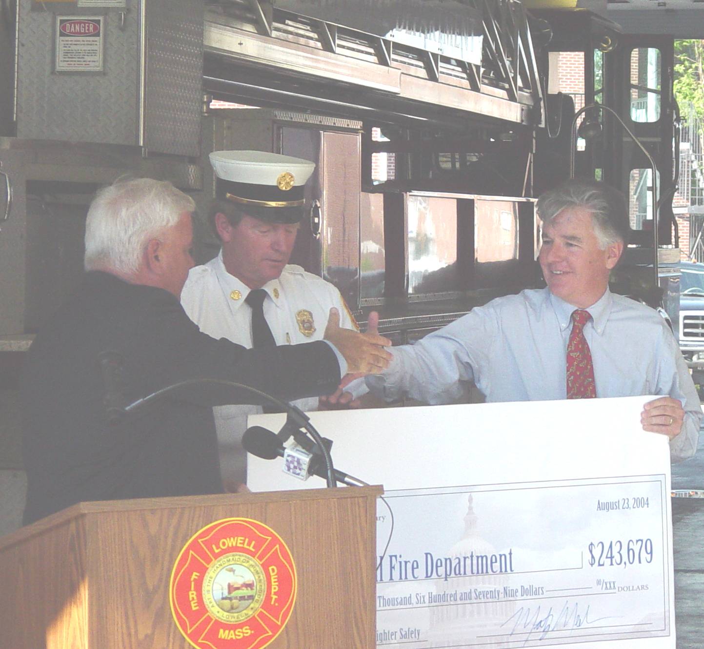 August 23, 2004: Lowell Fire Department Grant Announcement; The U.S. Department of Homeland Security awarded $243,679 for firefighter safety equipment. Congressman Meehan (right) hands check to Lowell Fire Chief William Desrosiers (middle) and shakes hands with City Manager John Cox (left).