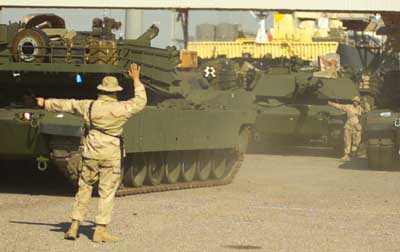 Two U.S. Marines guide the driver of an M1A1 Abrams tank into a staging area after the tank was offloaded from a Maritime Prepositioning Force ship at a port in Kuwait Jan. 17, 2003. The equipment being offloaded will be linked up with the Camp Pendleton, Calif., based I Marine Expeditionary Force, which is repositioning to the region in support of the global war on terrorism. One Maritime Prepositioning Force squadron carries enough equipment, ranging from food and ammunition to tanks and howitzers, to outfit 17,000 troops for 30 days. Photo by: Staff Sgt. Bill Lisbon