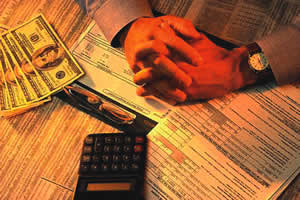 photo - folded hands on table with calculator, newspaper, cash