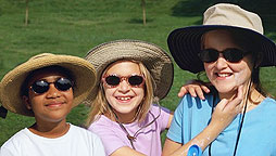 Photo of three girls wearing wide-brimmed hats, sunglasses and applying sunscreen.