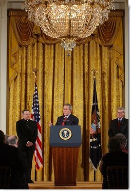 President George W. Bush addresses The National Catholic Educational Association in the East Room Friday, Jan. 9, 2004. Pictured with the President are Bishop Gregory Aymond of Austin, Texas, left and Michael Guerra, President of the NCEA. White House photo by Tina Hager.