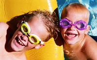 Two boys in colorful goggles play on a raft in a pool.