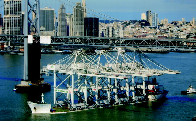 This picture shows a barge loaded with four construction cranes passing underneath the Oakland Bay Bridge with two feet of clearance.