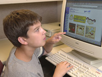 Photo of boy sitting in front of a computer pointing to the screen