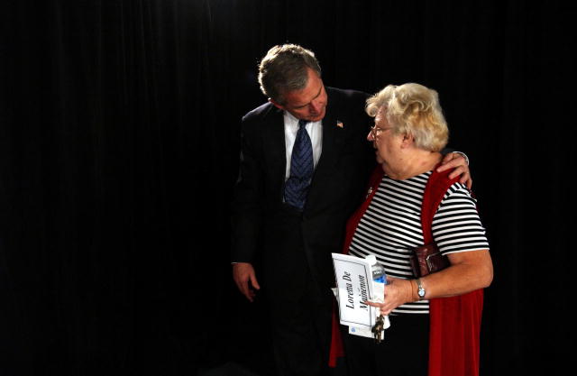 President Bush and a senior woman speak privately in front of black backdrop.