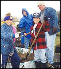 Two children and two adults working outdoors with shovels.