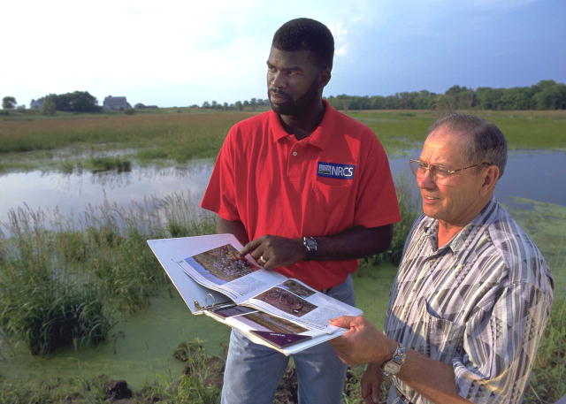 Farmer and NRCS specialist discussing wetland conservation near a pond.